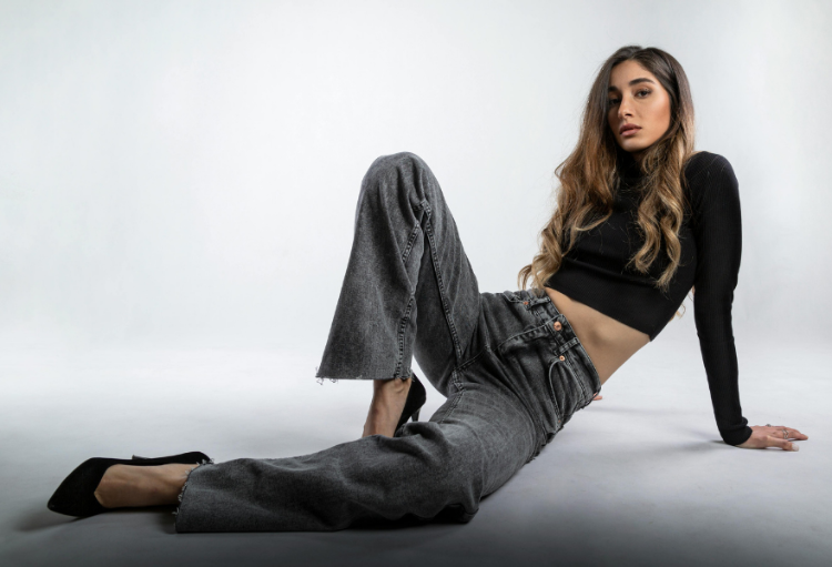 Woman sitting on the floor wearing a black top and gray pants against a white background