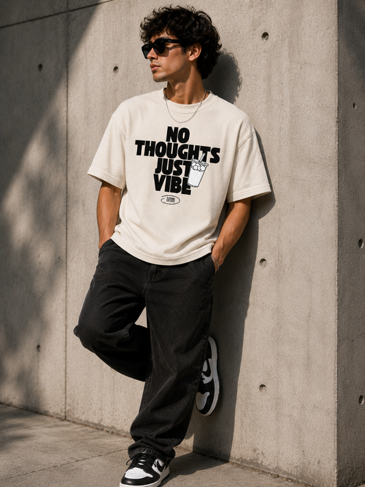Person wearing a white t-shirt with text leaning against a concrete wall.